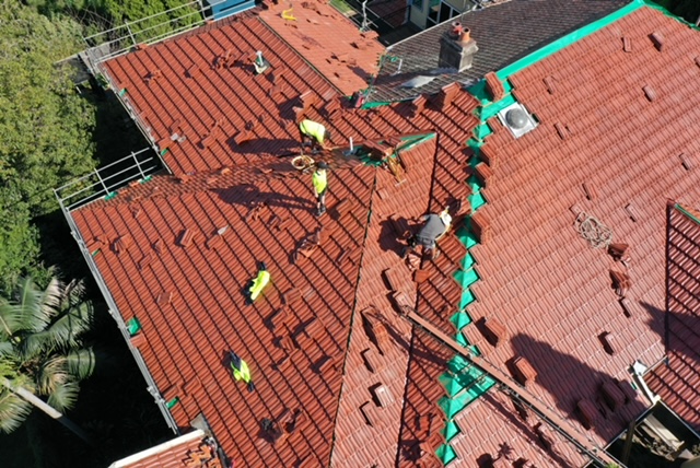 Aerial view of workers replacing tiles on a red terracotta roof.