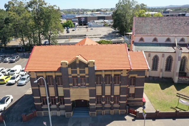 Aerial shot of a two-storey brick heritage building with a newly tiled orange roof, located next to a church.