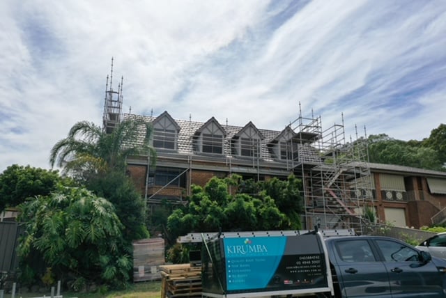 Two-storey brick house undergo roof work surrounded by scaffolding, with a work truck parked in front.