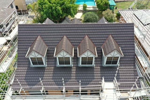 Aerial view of a house with dark brown roof tiles, four dormer windows, and surrounding scaffolding.