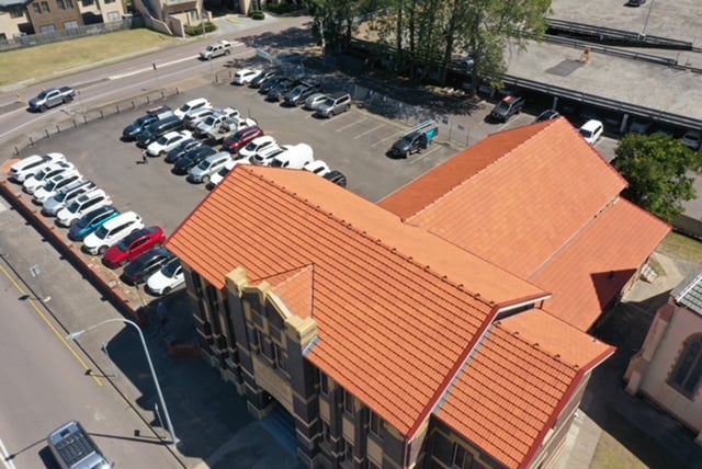 High-angle aerial view of a building with a newly installed orange tiled roof next to a parking lot.
