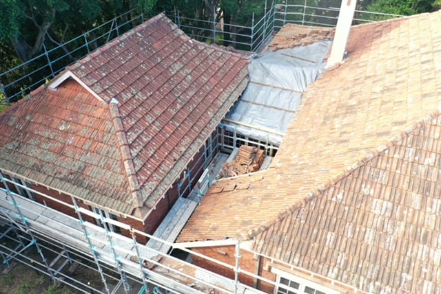 Aerial view of an old tile roof undergoing restoration with surrounding scaffolding and protective tarping.