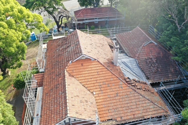 High-angle aerial view of a tiled house roof surrounded by scaffolding during a roofing renovation project.