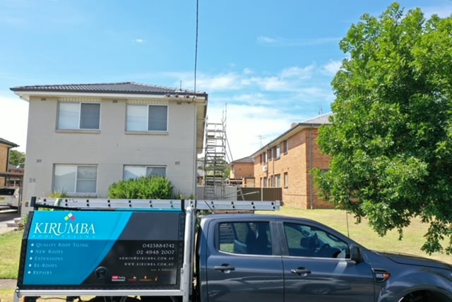 Ground-level view of a roofing company ute parked outside a two-storey residential building with scaffolding set up.