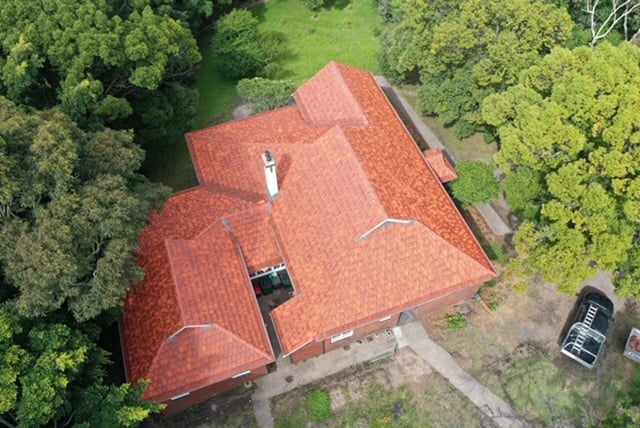 Direct overhead aerial view of a large house with a new orange-red tiled roof, nestled among dense trees.